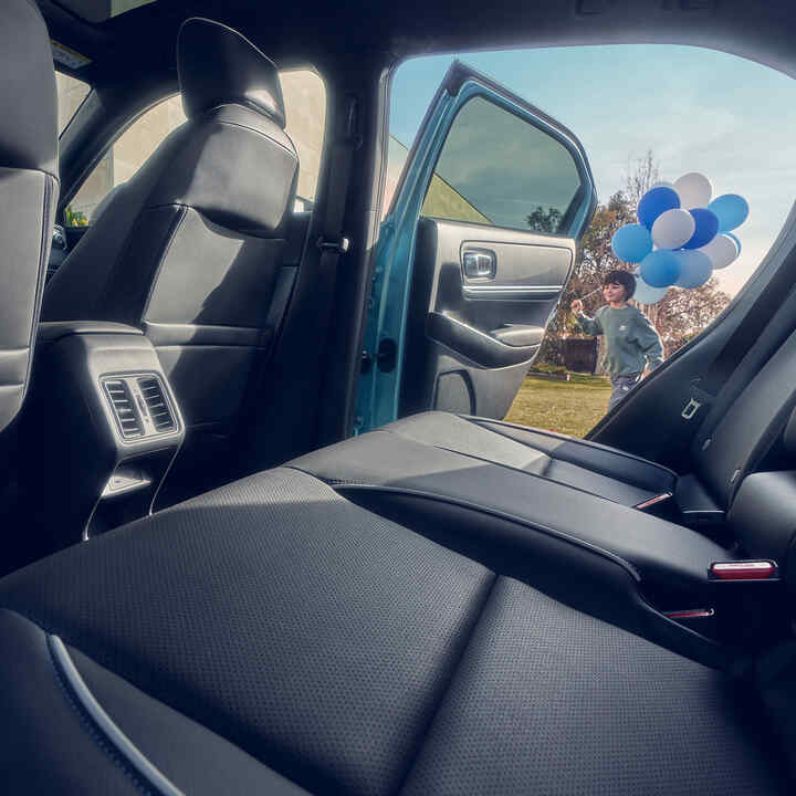 Nærbillede af bagsædet i Honda e:Ny1 med et barn, der går med balloner forbi åben dør.