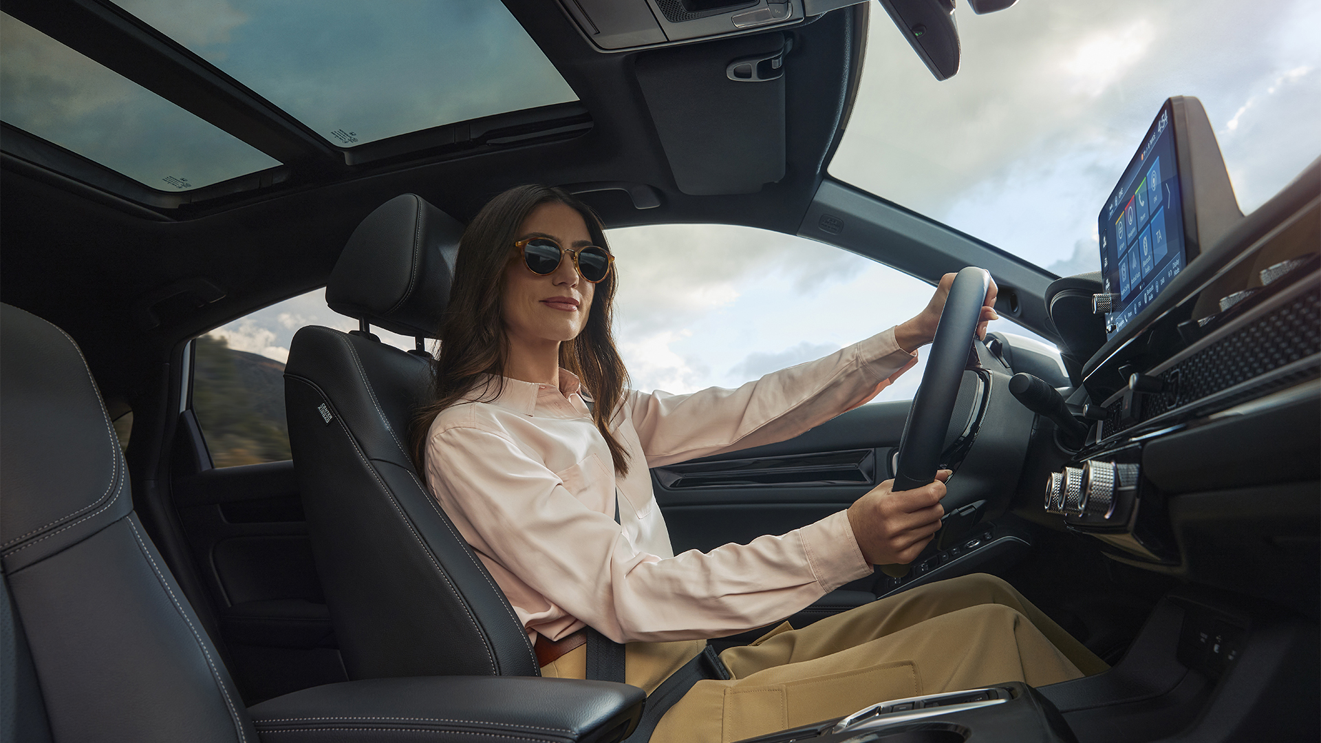 A woman in sunglasses, with her hands on the Civic Hybrid's steering wheel