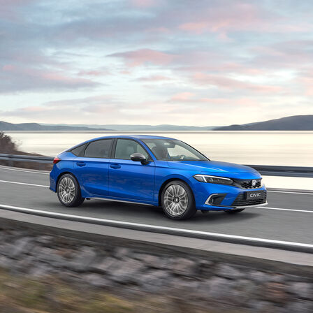 Honda Civic e:HEV, som kører ned ad en kystvej, set skråt forfra.