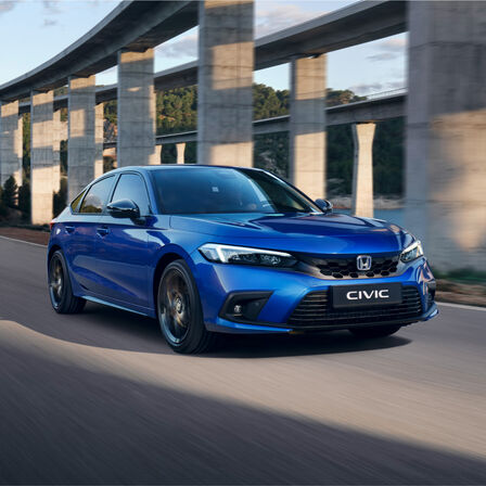 front facing three quarter Honda Civic e:HEV hatchback driving down the road.
