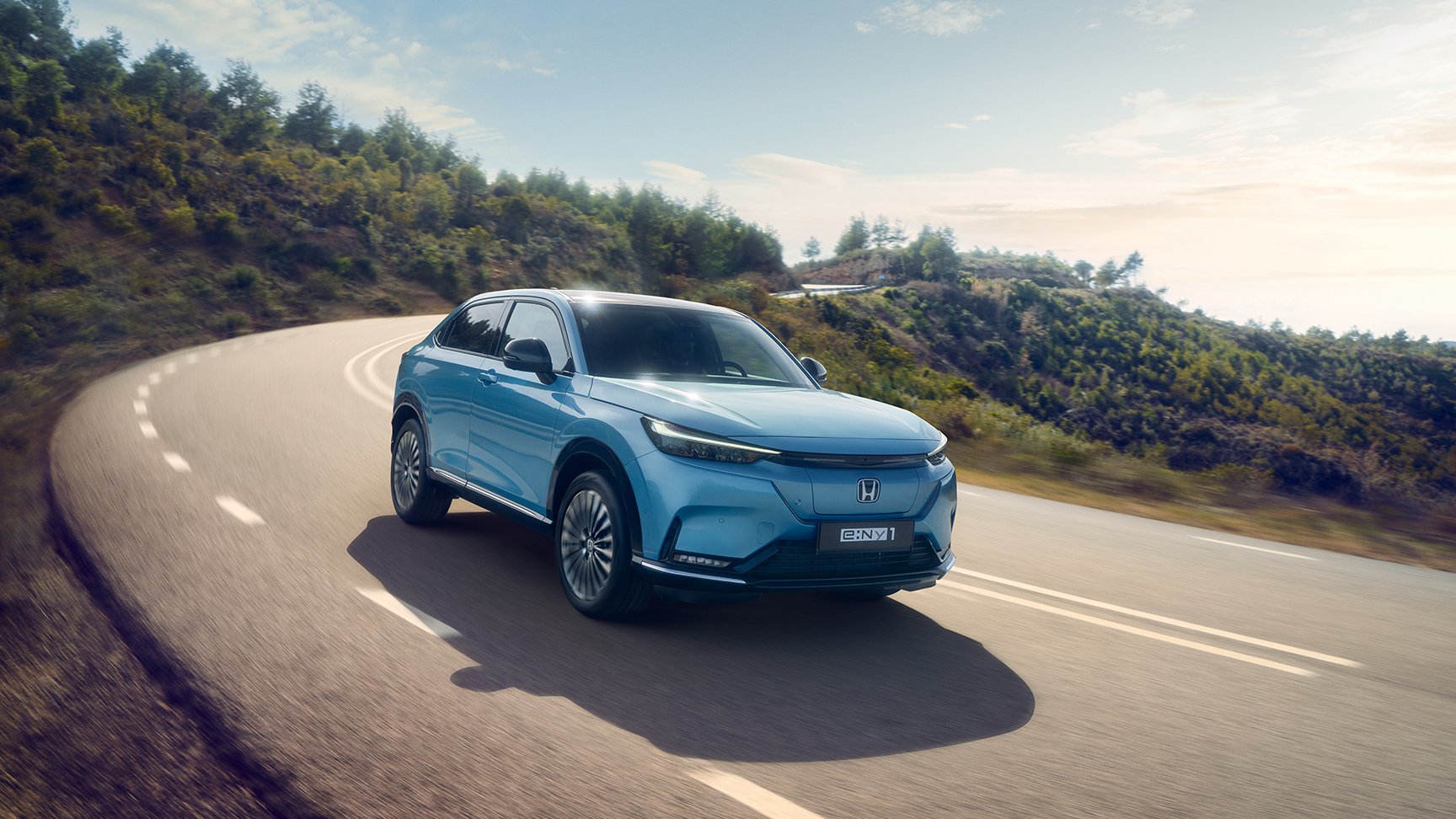 Honda e:Ny1, som kører ned ad vejen i et landområde, set forfra.