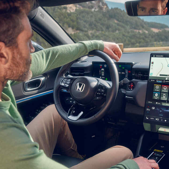 Mand, der kører i Honda e:Ny1 og bruger navigation på det digitale førerdisplay.