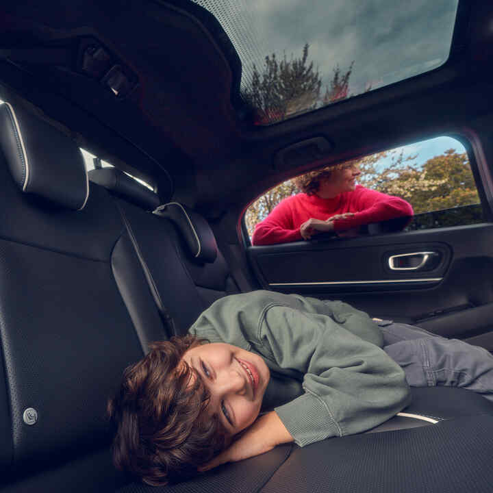 Barn ligger på bagsædet, mens mor står i vinduet på Honda e:Ny1.