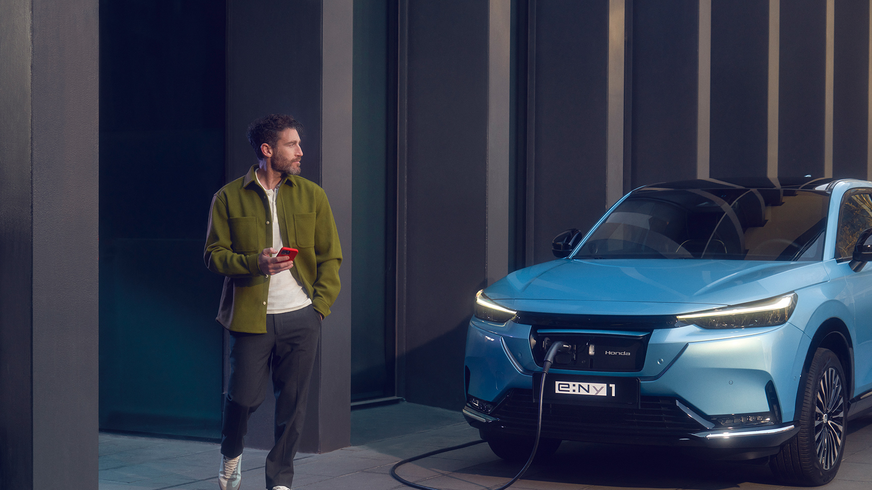 Mand, der går forbi en Honda e:Ny1, som bliver ladet op foran en bygning.
