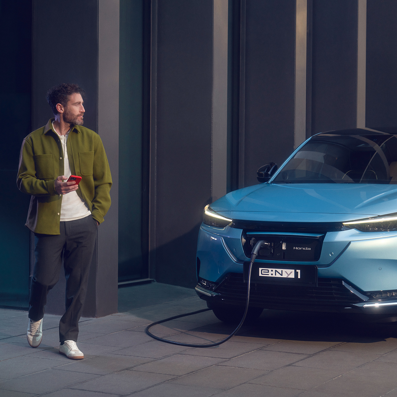 Mand, der går forbi en Honda e:Ny1, som bliver ladet op foran en bygning.