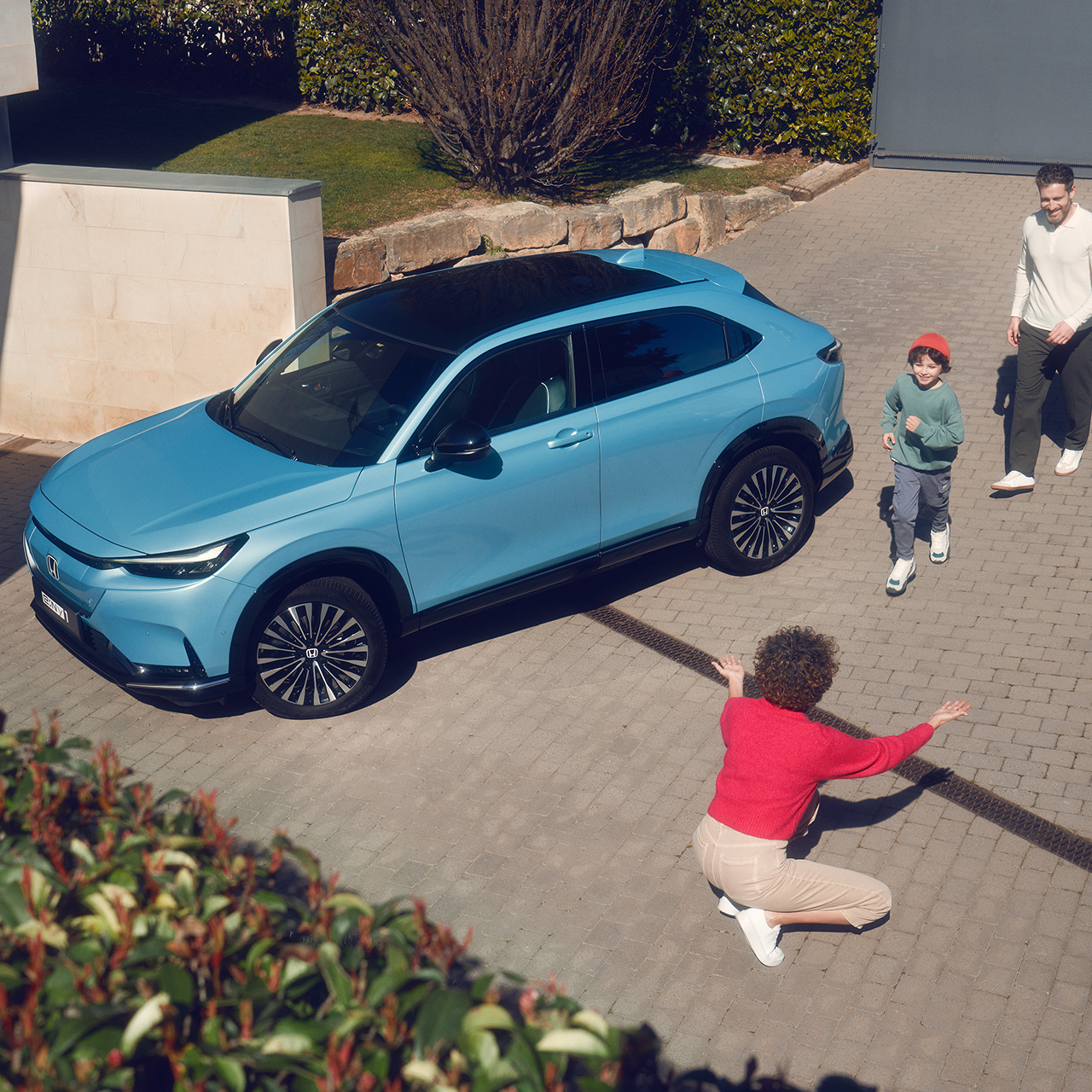 Familie omkring en parkeret Honda e:Ny1 i en indkørsel.