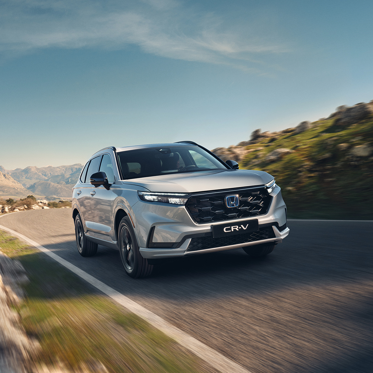 Hvid CR-V Plug-in Hybrid, der kører på vejen i et bjergområde.