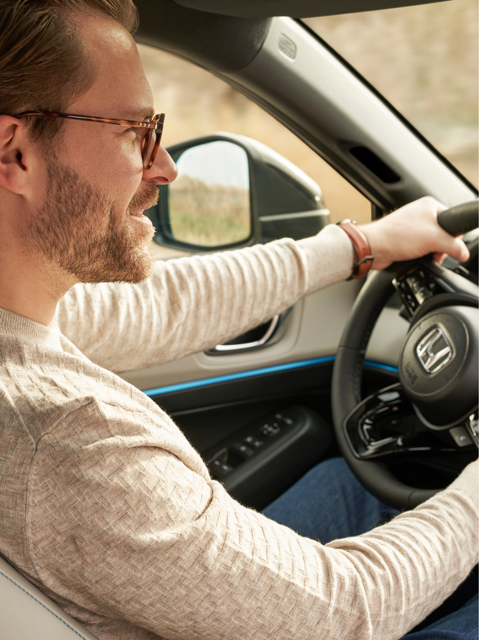 En mand med briller kører en Honda HR-V, set fra passagerpladsen foran, med begge hænder på rattet og instrumentbrættet tydeligt synligt.