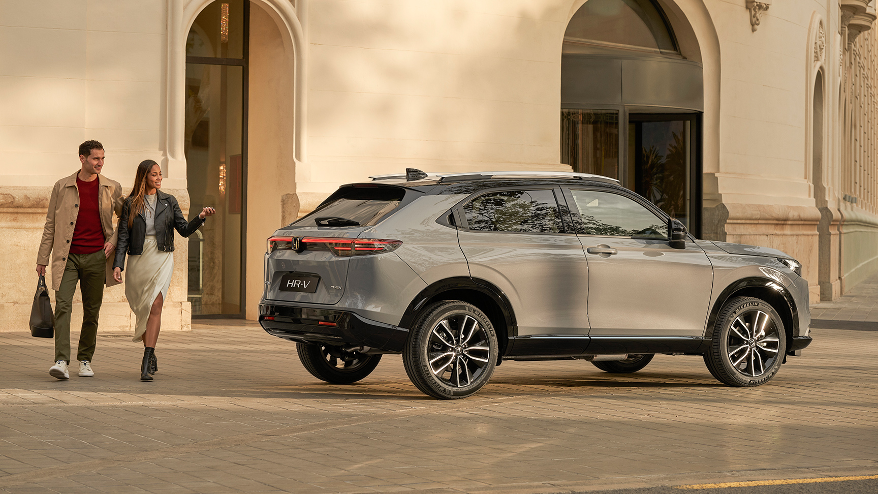 Par går ved siden af ​​HR-V, der er parkeret uden for en bygning. 