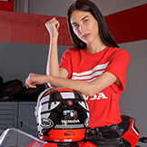 Dame iført en rød Honda-top læner sig op ad en Honda-motorcykelhjelm.