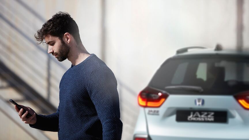 En dame, der står ved siden af White Honda e og bruger My Honda Plus-appen