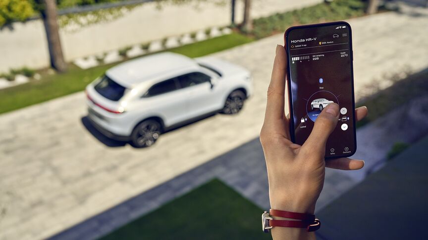 En dame, der står ved siden af White Honda e og bruger My Honda Plus-appen