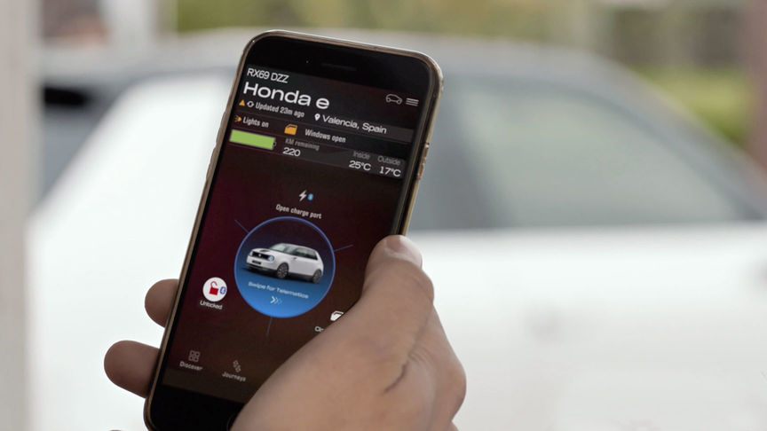 En mand, der ser på My Honda Plus-appen med Honda Jazz Hybrid Crosstar bagved. 