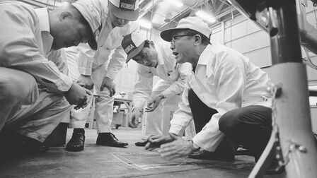 Soichiro Honda og nogle fabriksarbejdere i hvide overalls.