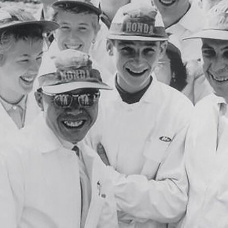 Soichiro Honda og nogle fabriksarbejdere i hvide kedeldragter.