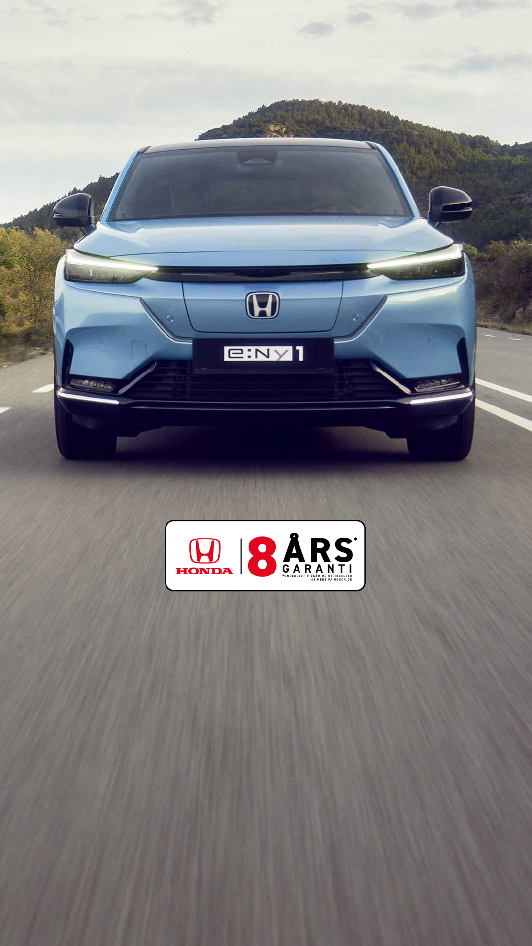 Honda e:Ny1 i Aqua Topaz Metallic kører på en snoet vej med grønne bakker i baggrunden.